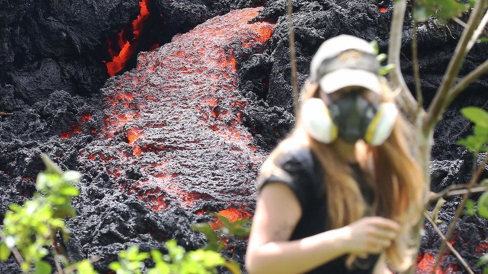 MAY 12: Lava flows at a new fissure in the aftermath of eruptions from the Kilauea volcano on Hawaii's Big Island as a local resident walks nearby after taking photos on May 12, 2018 in Pahoa, Hawaii. The U.S. Geological Survey said a recent lowering of the lava lake at the volcano's Halemaumau crater Òhas raised the potential for explosive eruptionsÓ at the volcano. Authorities have confirmed the fissure is the 16th to open. (Photo by Mario Tama/Getty Images)