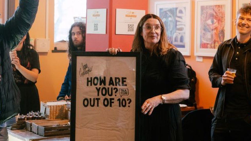 A woman holding an artwork with the words 'How are you? Out of 10?'