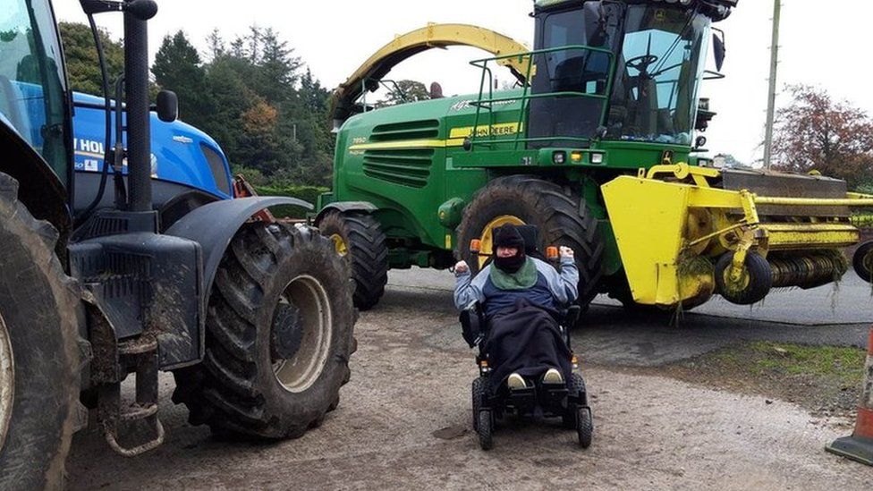 Jonathan Turtle in his wheelchair beside a tractor and a combined harvester