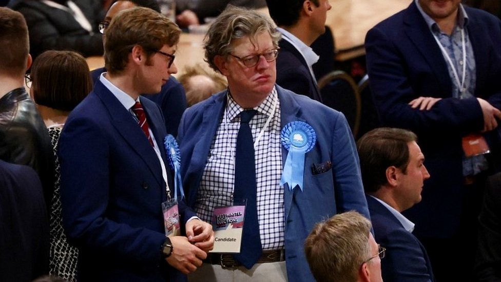 Two candidates wearing rosettes of the Conservative party stand during an announcement amidst the counting process at the Westminster City Council local elections