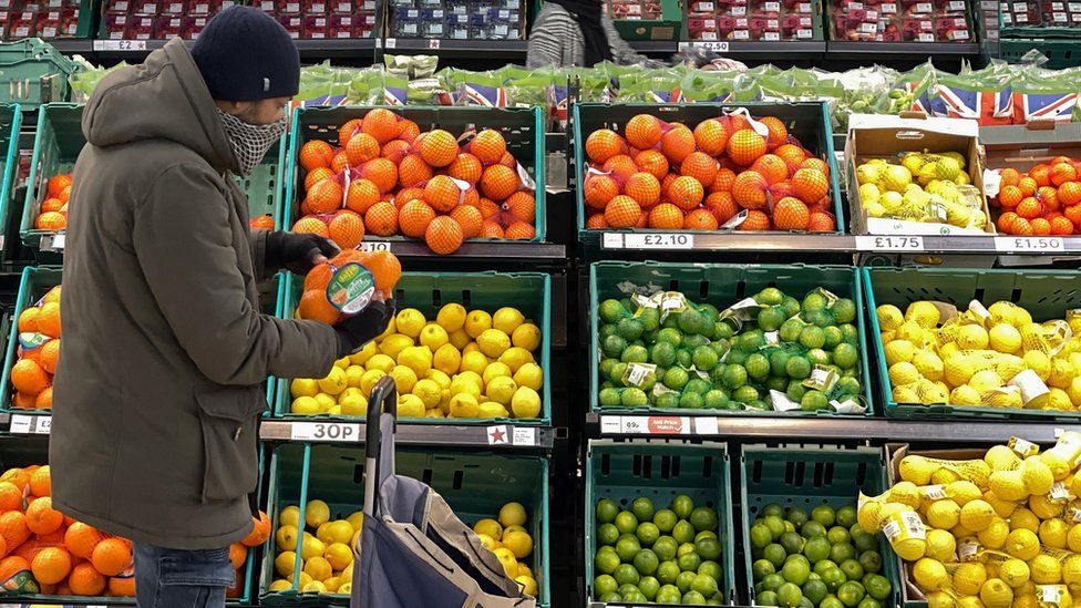 A man shopping at a grocery store holding oranges