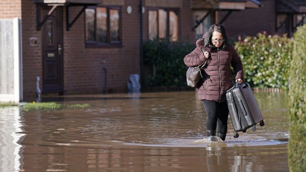 A resident with a suitcase walks through flood water in Retford