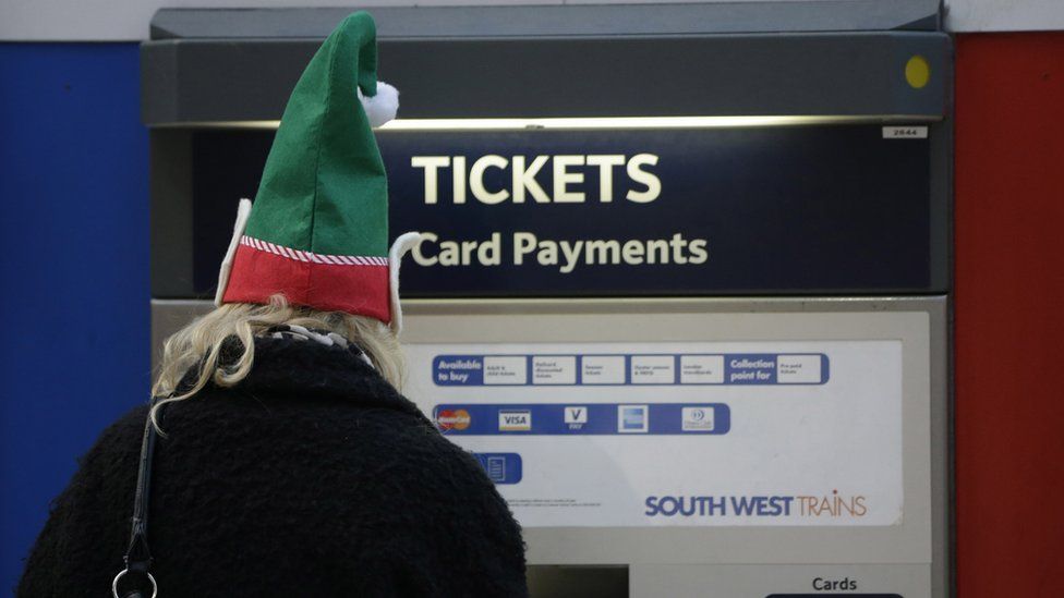 A traveler wears a festive hat as they use a self-service ticket machine at Waterloo railway station, in London,