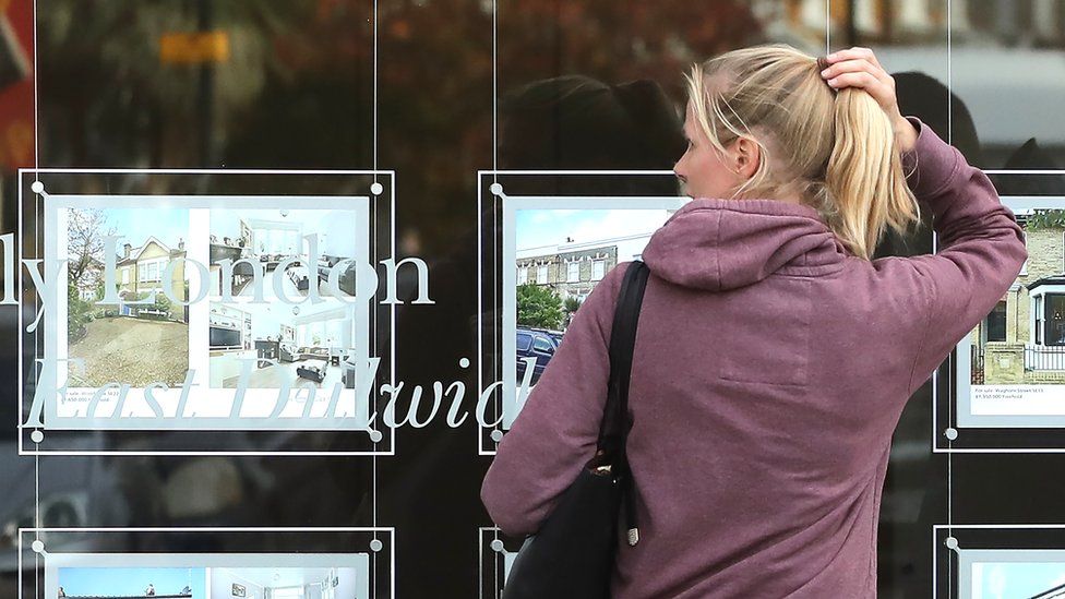 A young woman looks at housing options through an estate agents' window