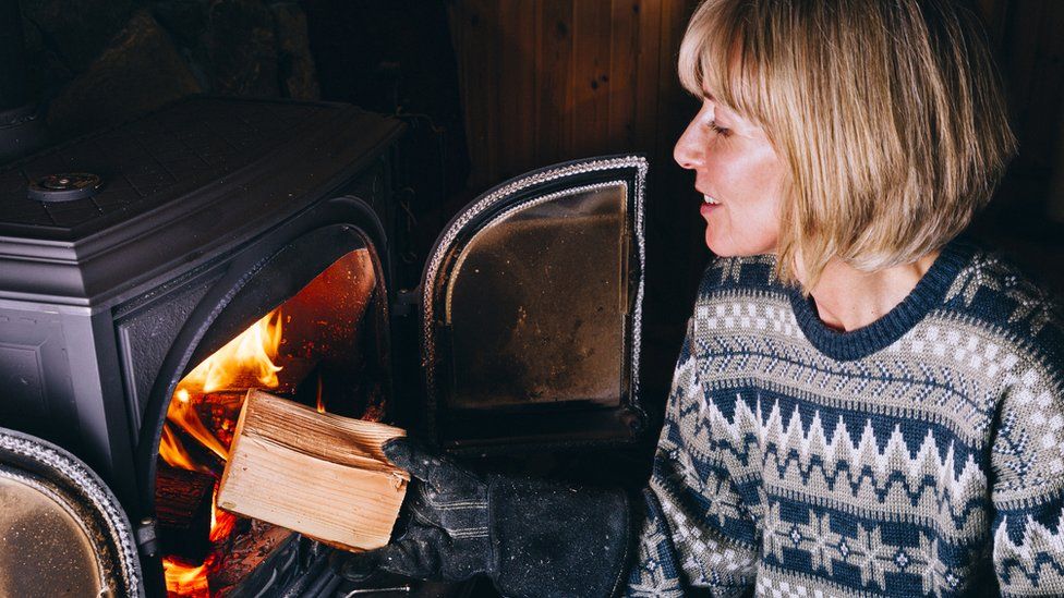 Woman putting logs in a wood burning stove - stock photo
