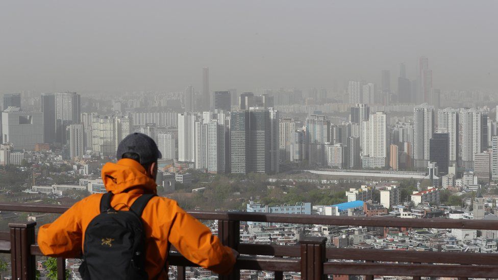 Man looks at Seoul skyline shrouded in yellow dust