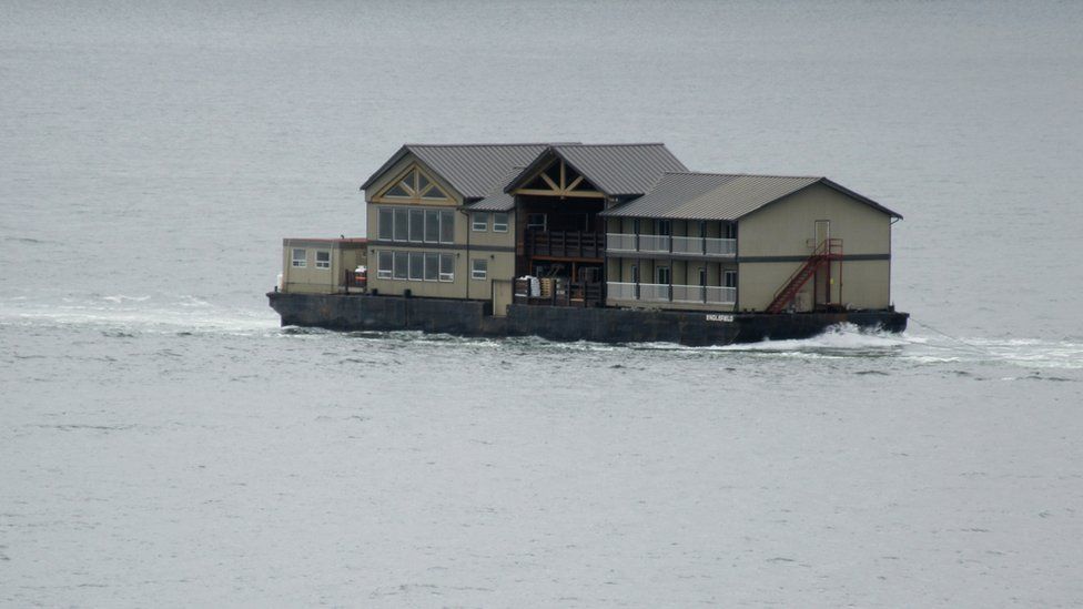 A fishing lodge is being towed across a river