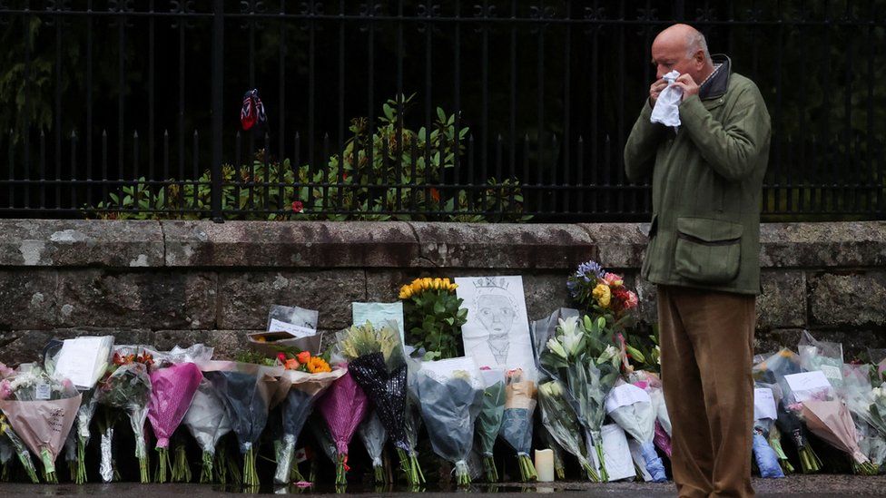 A man wipes away tears floral tributes by an entrance to Balmoral Castle