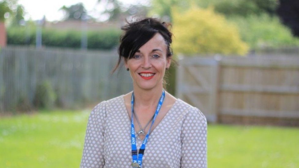 Woman with very dark hair wearing an NHS lanyard