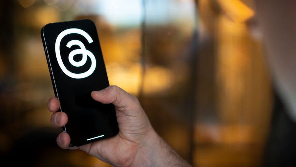 A stock photo of someone holding a phone with the Threads logo on screen