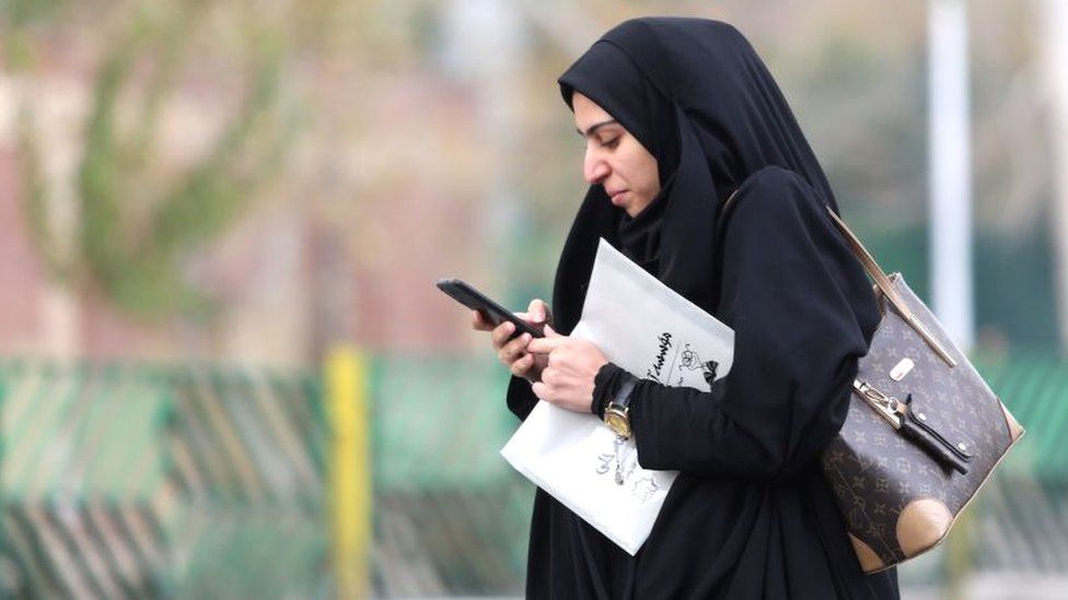 A woman in Tehran with a newspaper looking at her mobile phone