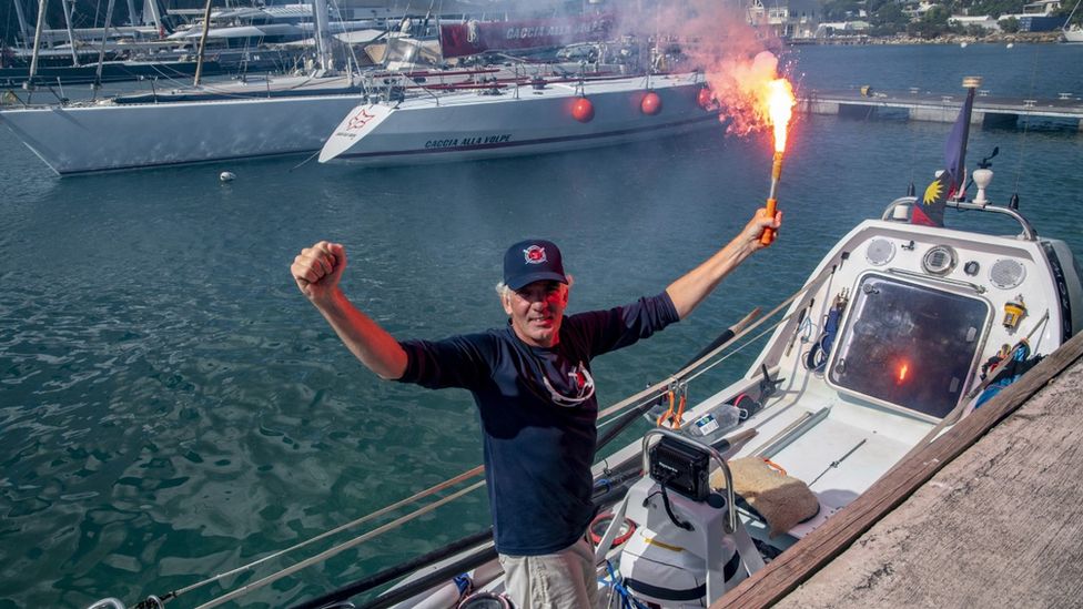 Andrew Osborne with his arms up holding a flare on his boat