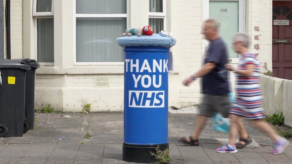 People walk past NHS themed post box outside shabby house