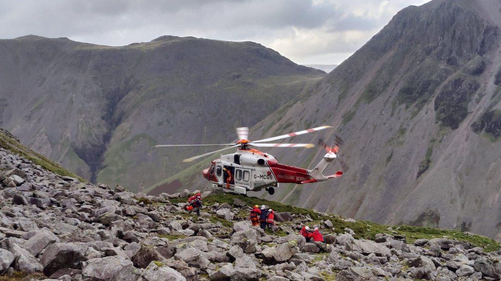 Volunteers help a casualty walk to as helicopter hovering among steep hills
