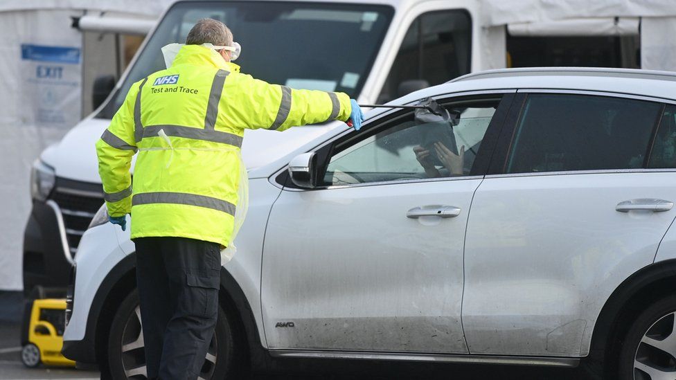 An NHS Test and Trace employee uses a litter picker to hand testing kits through car windows to people arriving at a drive through testing site at a former Park and Ride location in Southport, north west England, on February 3, 2021