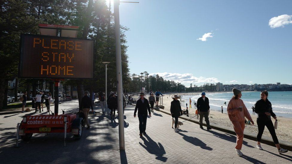 A sign saying 'Please stay home' beside a beach