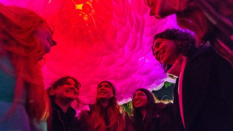 A group of young women standing and looking up at a big pink flower glowing above them