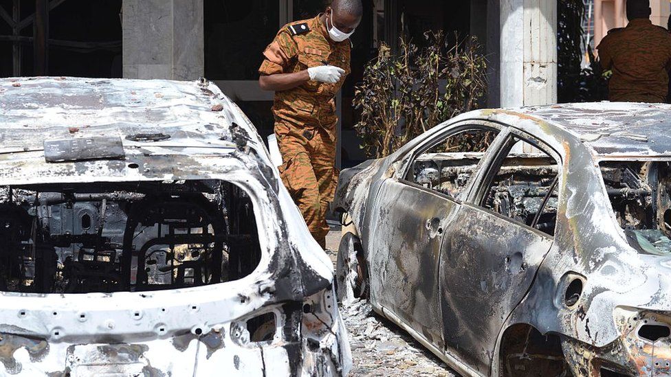 A Burkinabe investigator walks next to burnt cars in front of the Splendid hotel, on 17 January 2016 in Ouagadougou, following a jihadist attack