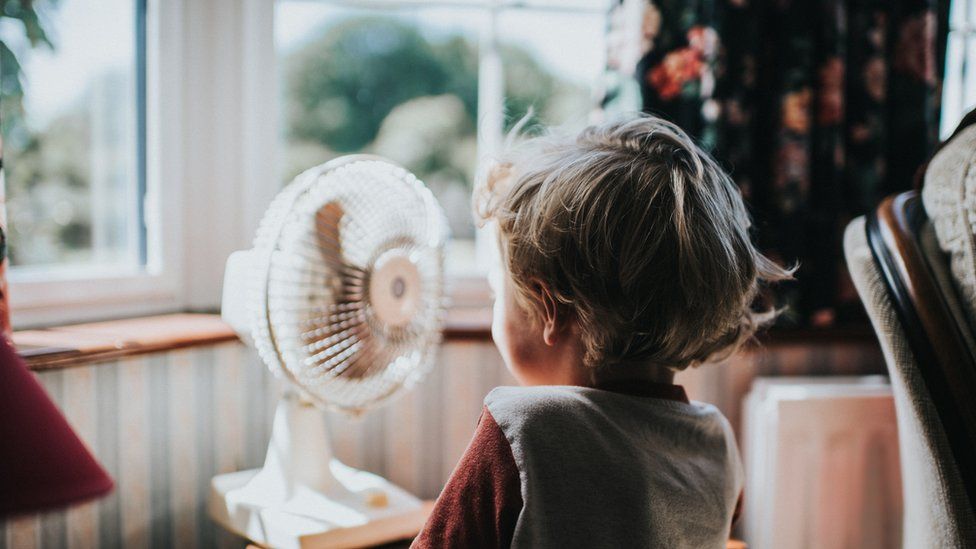 A photo of child in front of a window and an electric fan