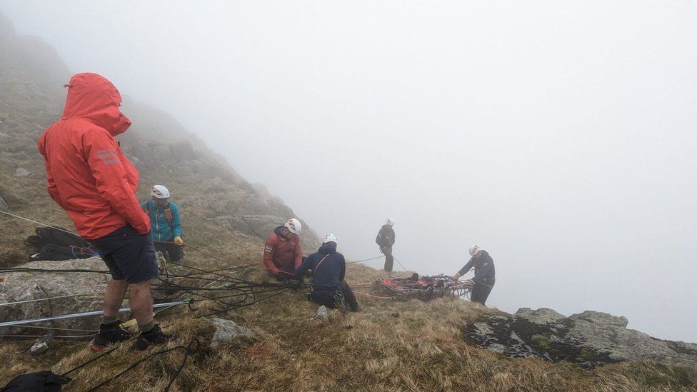Rescuers prepare to lower a stretcher down the fell using ropes