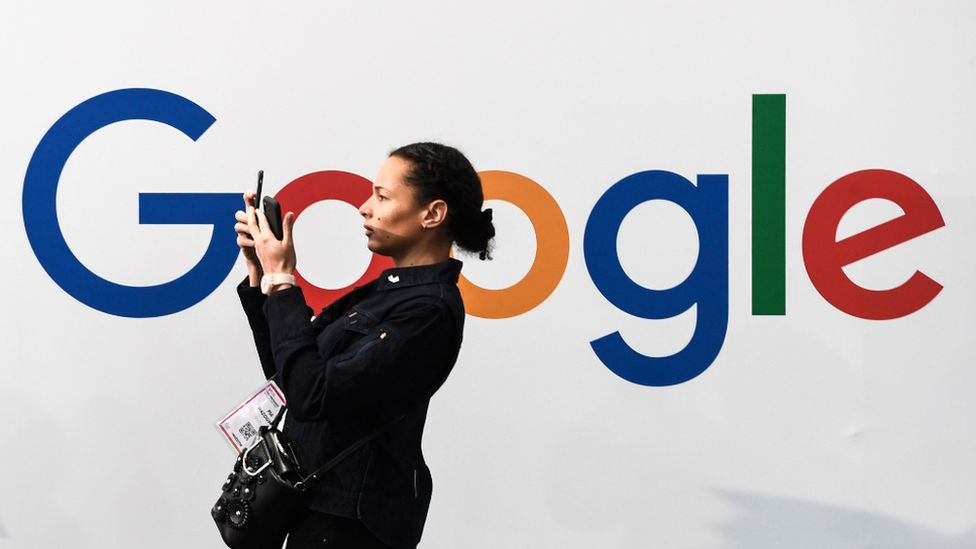 A woman uses her phone in front of a Google billboard