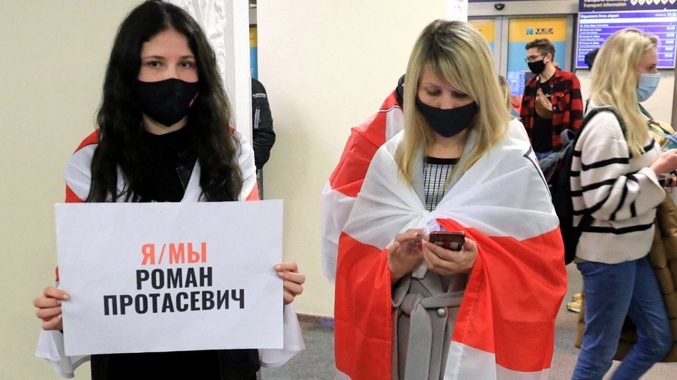 A young woman stands with a poster reading: "I am, we are Roman Protasevich" and the Belarus flag as passengers disembark from a Ryanair passenger plane from Athens, Greece