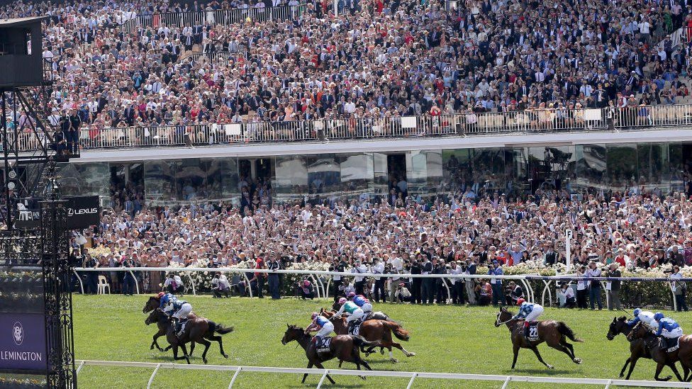 Thousands of race-goers in the stands at Flemington Racecourse watch horse gallop down the final leg of the Melbourne Cup race.