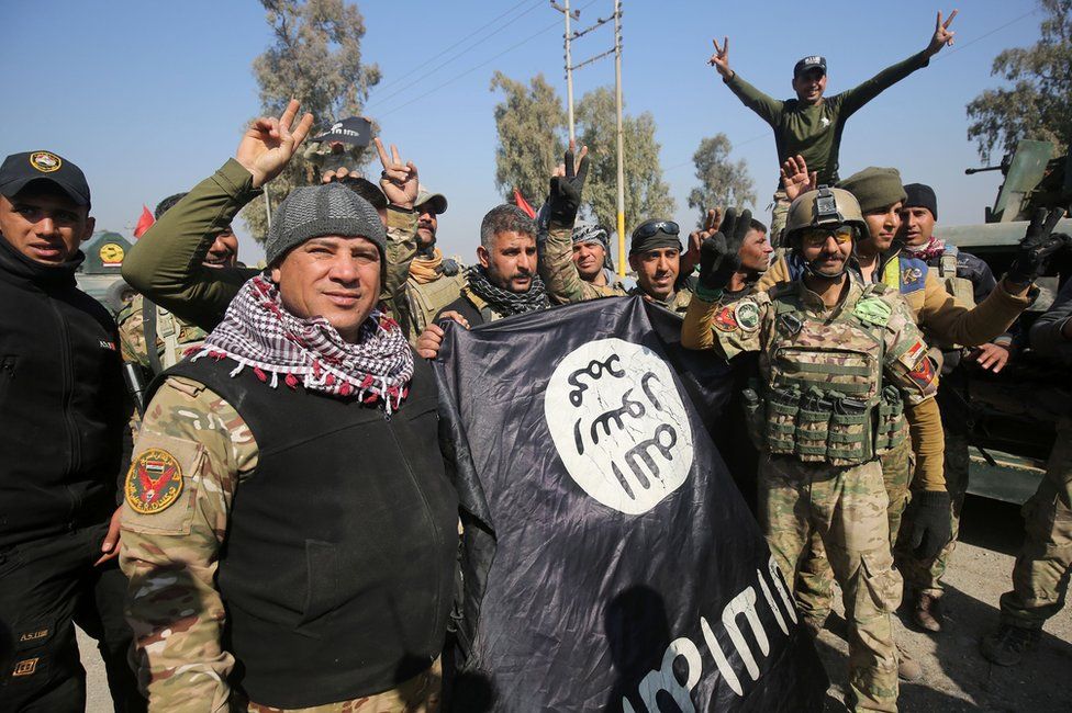Iraqi soldiers flash victory signs and brandish an IS flag after entering Mosul airport, 23 February