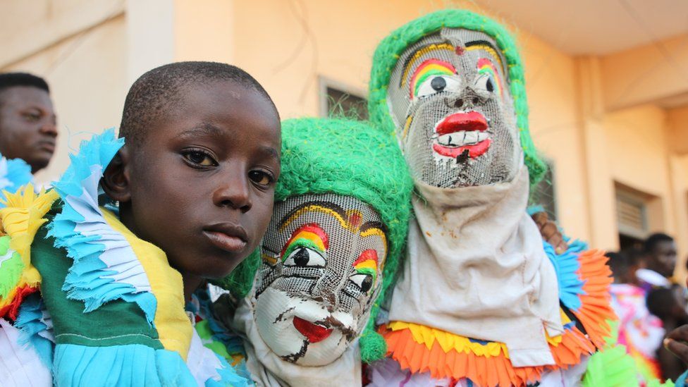 Three children pose, two of them with their faces fully covered by masks and green wigs in Sekondi Ghana