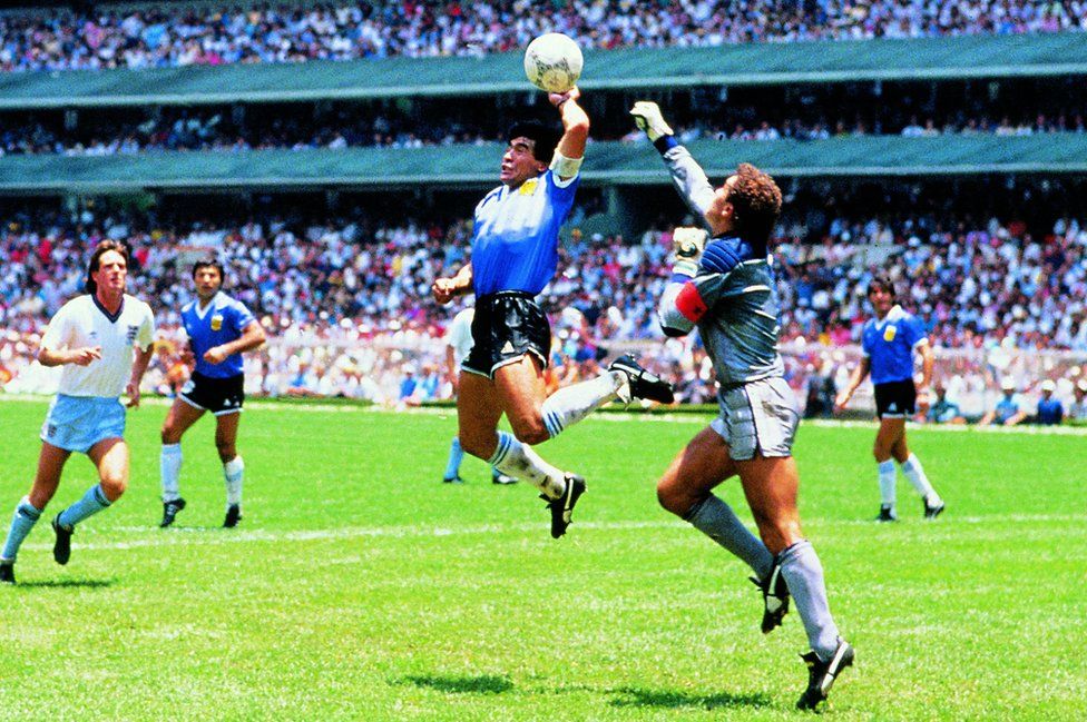 Diego Maradona handling the ball ahead of an approaching Peter Shilton