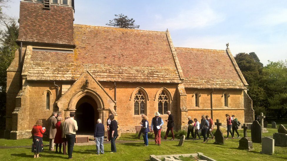The exterior of an historic church showing people in the graveyard