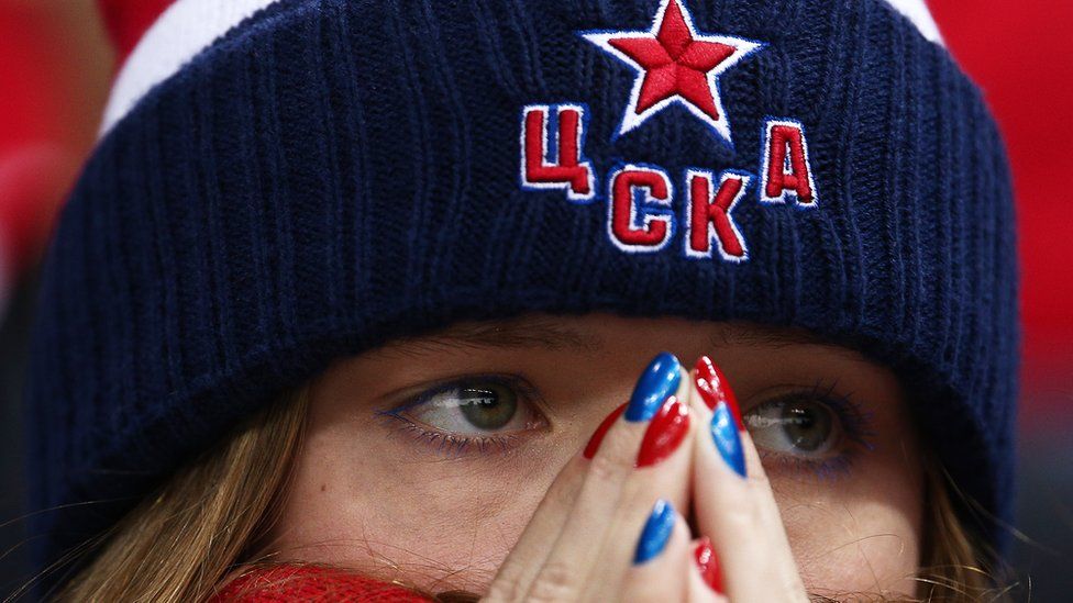A close-up of a Russian football fan. She has her nails painted Russia colours and looks on with worry.