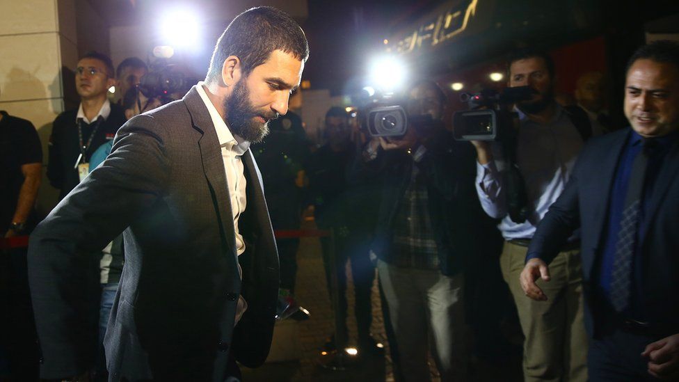 Arda Turan wearing a suit, flanked by papparazi in 2016