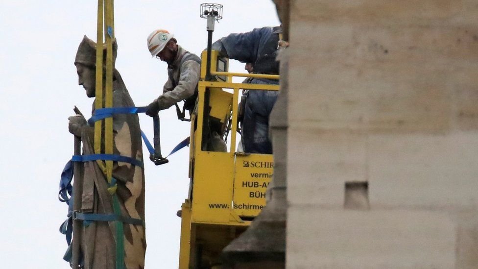 Men work on a statue on a facade at Notre-Dame Cathedral