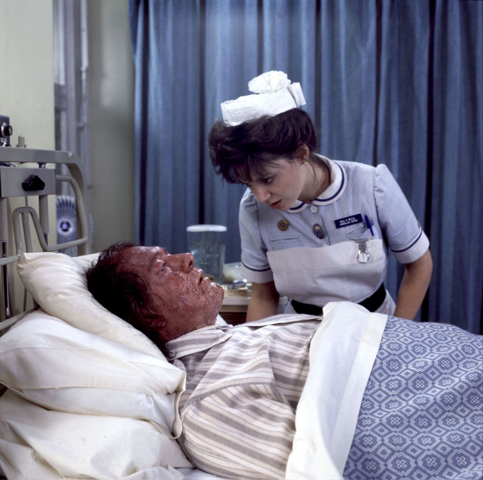 Майкл Гэмбон в роли Филипа Марлоу и Джоан Уолли в роли медсестры Миллс на его больничной койке, Марлоу страдает псориазом