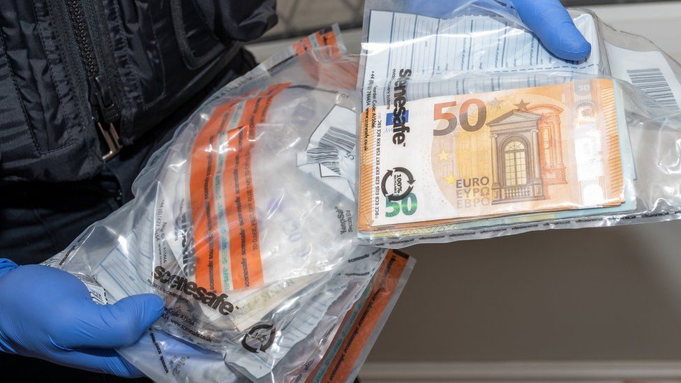 A police officer holding euro cash that has been placed in a bag