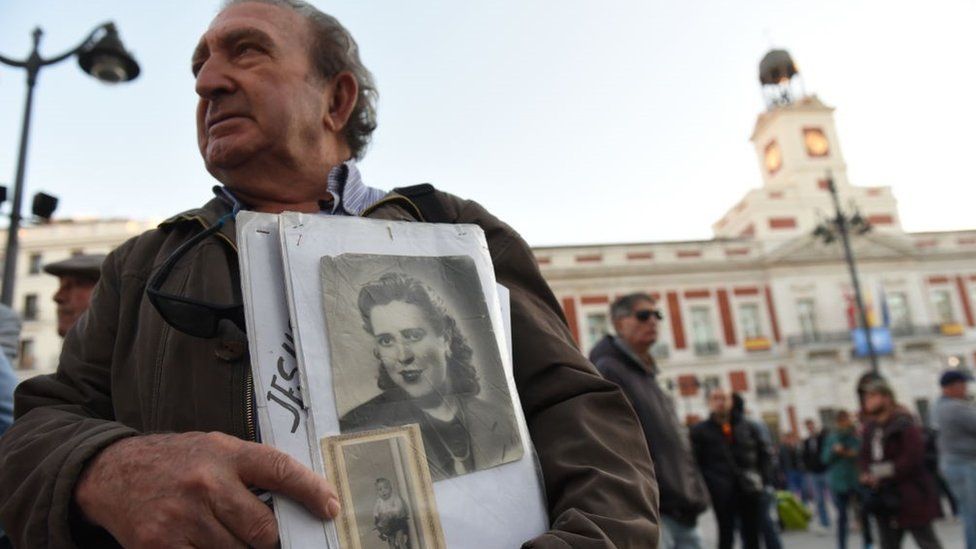 A man holds a picture of a woman who went missing under Franco