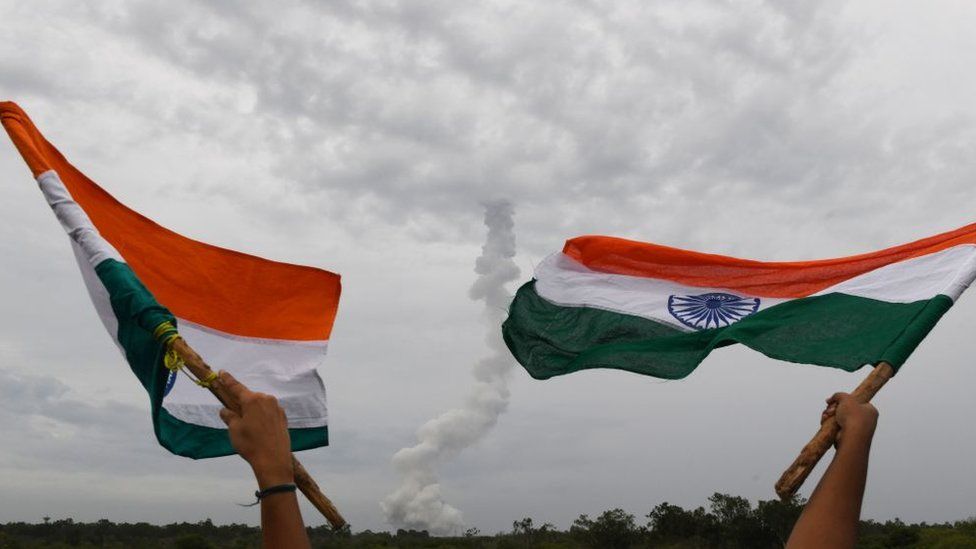Indian residents wave Indian national flags as The Indian Space Research Organisation's (ISRO) Chandrayaan-2 (Moon Chariot 2), on board the Geosynchronous Satellite Launch Vehicle (GSLV-mark III-M1), launches in Sriharikota in the state of Andhra Pradesh on July 22, 2019