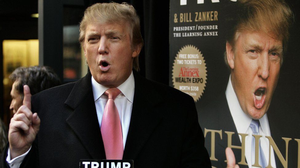 Donald Trump poses in front of a banner for his book