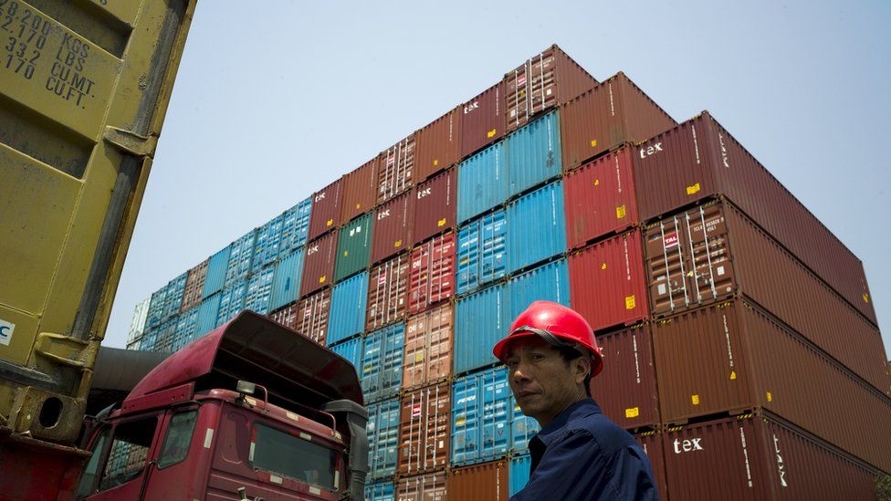 A worker stands in front of shipping containers