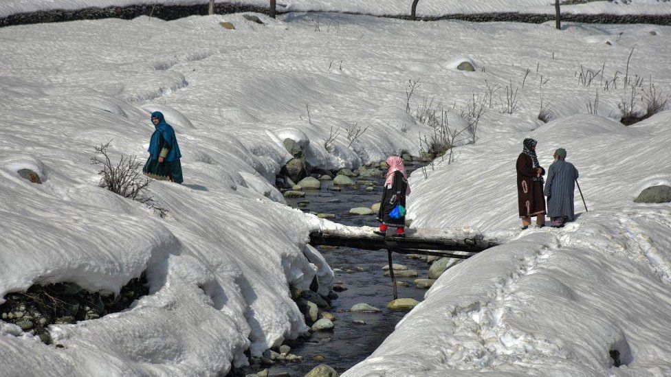 TANGMARG, KASHMIR, INDIA - 2023/02/15: Residents cross the snow covered foot-bridge during a sunny winter day in Tangmarg, about 50kms from Srinagar, the summer capital of Jammu and Kashmir.
