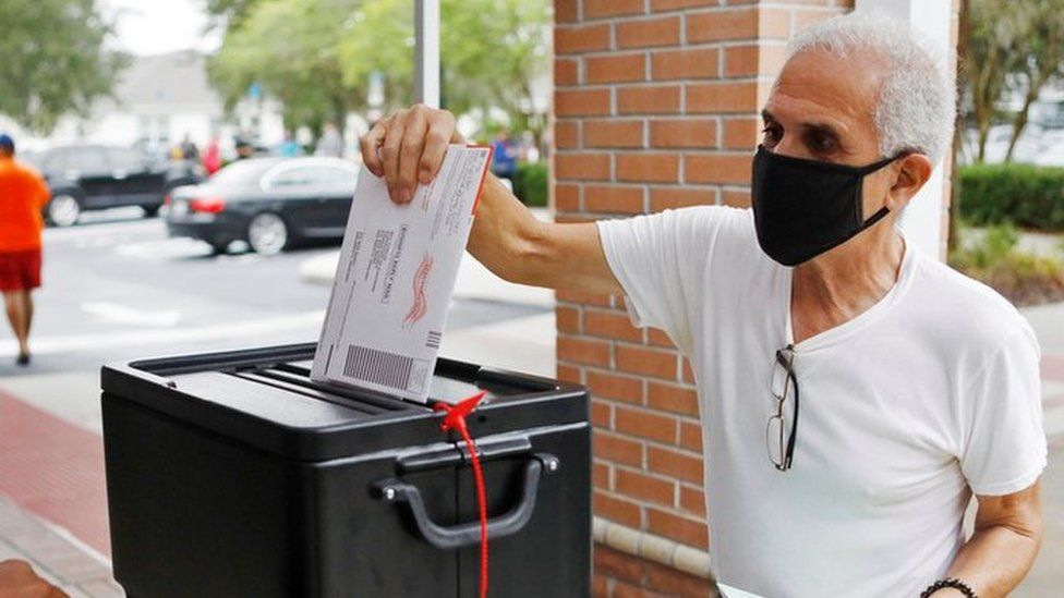 Man in a black face mask returns his mail-in ballot