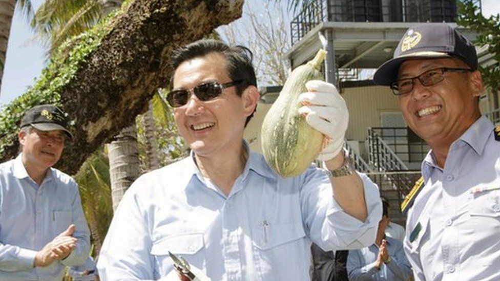 President Ma Ying-jeou holding up a fruit, and flanked by officials