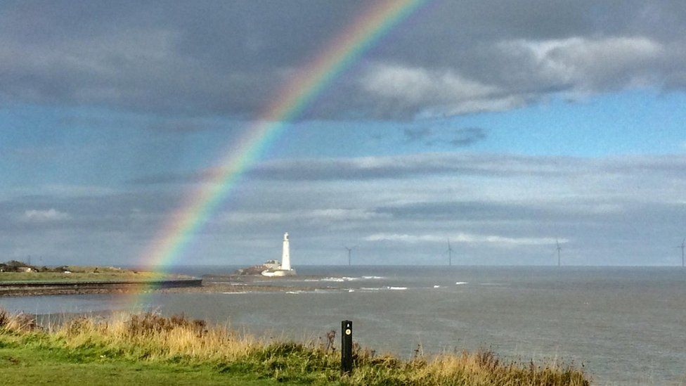 Rainbow over a white lighthouse by the coast