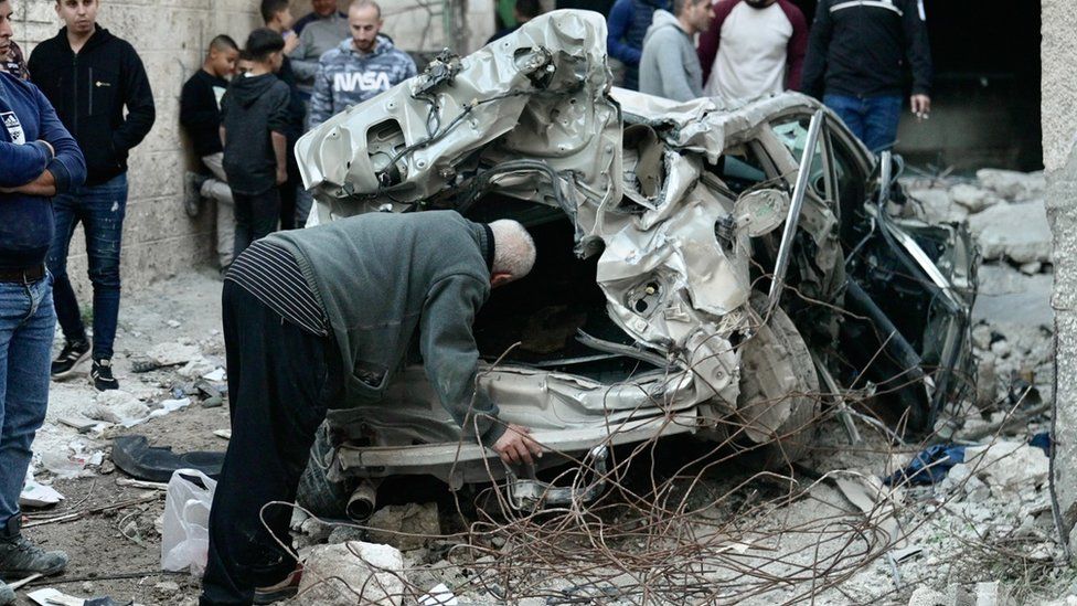 Palestinians inspect a destroyed car in Jenin, in the occupied West Bank, following an Israeli military raid (29 November 2023)