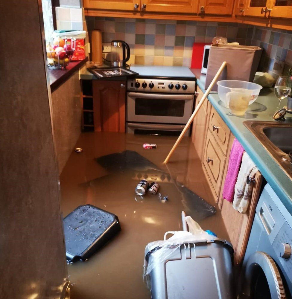 The kitchen flooded, with bins and rubbish floating in brown water, partially submerging the cooker