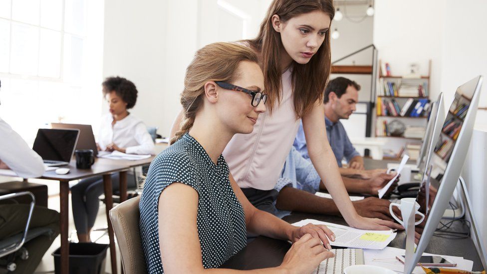 Two women chatting in an open plan office