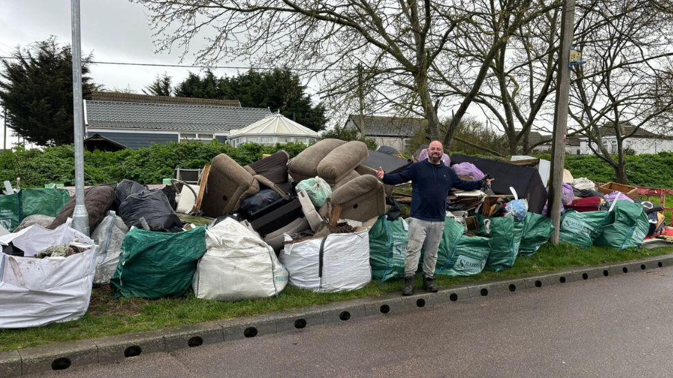 Bradley Thompson stood in front of fly tipping and collected litter