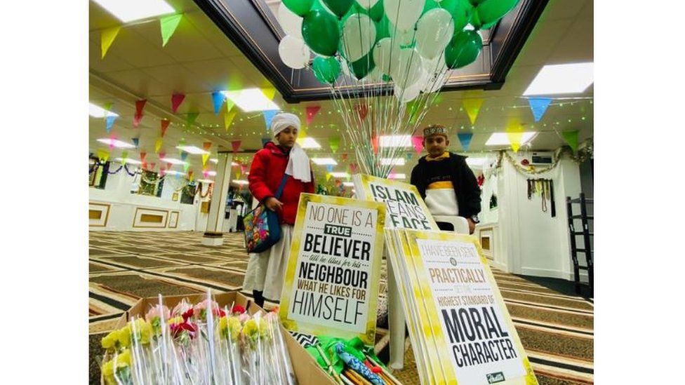 Two children stand by a pile of placards and flowers inside the Easton Jamia Mosque