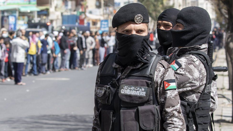 Jordanian security forces look on as people queue for bread in Amman (24 March 2020)